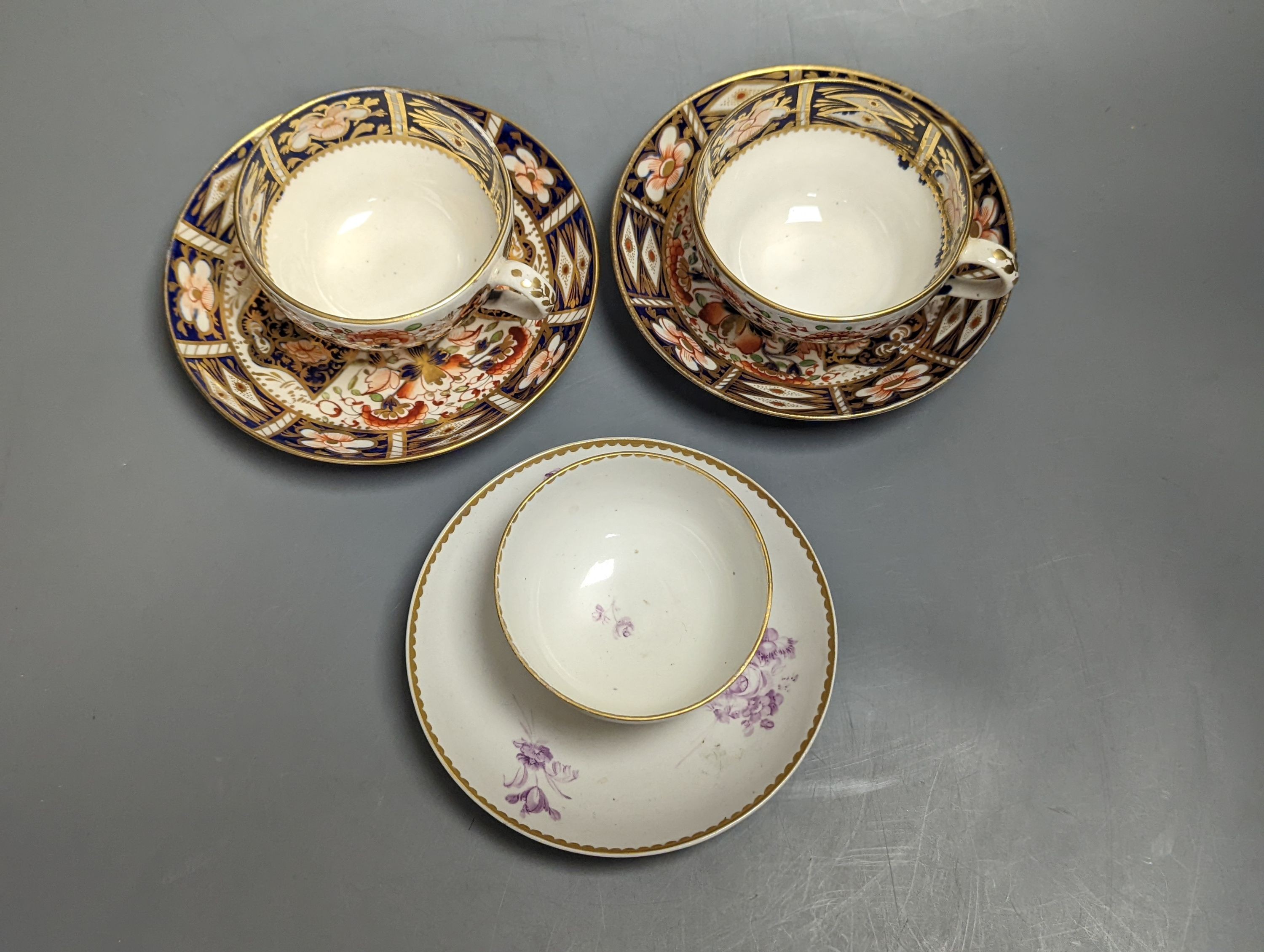 Two Derby imari pattern tea cups and saucers and a Derby teabowl and saucer painted in puce, each with three sprays of flowers, c.1785 and later